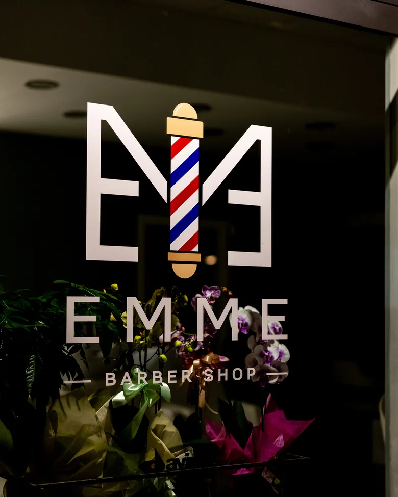 L'insegna di EMME Barber Shop illuminata di sera in Via Bardet a Pescara